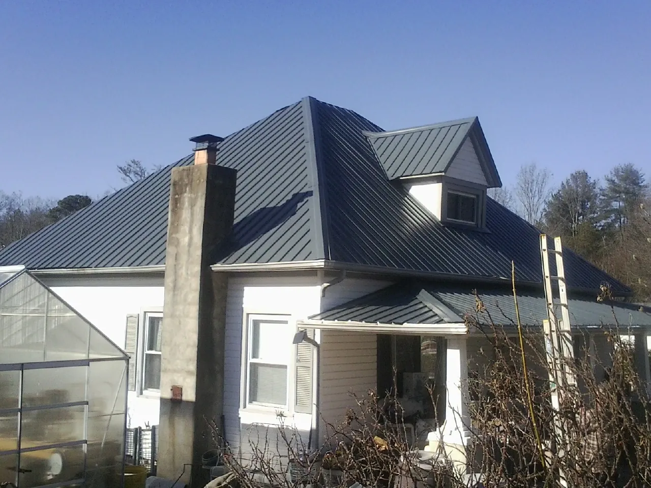 Dark blue standing seam metal roof on a white farmhouse with dormer — Slate & Tile Roof Repair by Roofing Brothers in Champion
