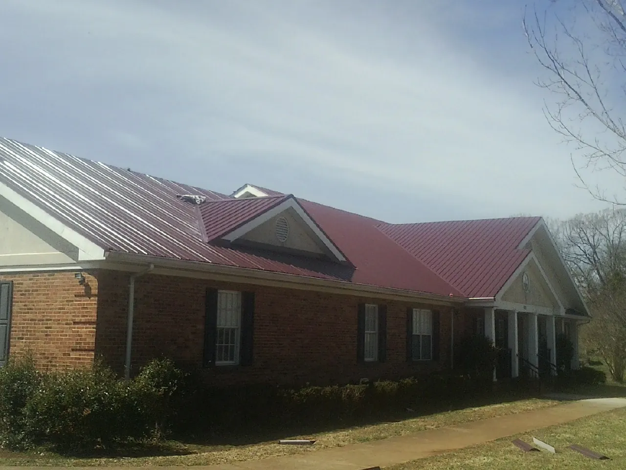 Red metal roof with gabled entries on a long brick building, from a Hail Damage Roof Repair job in Champion