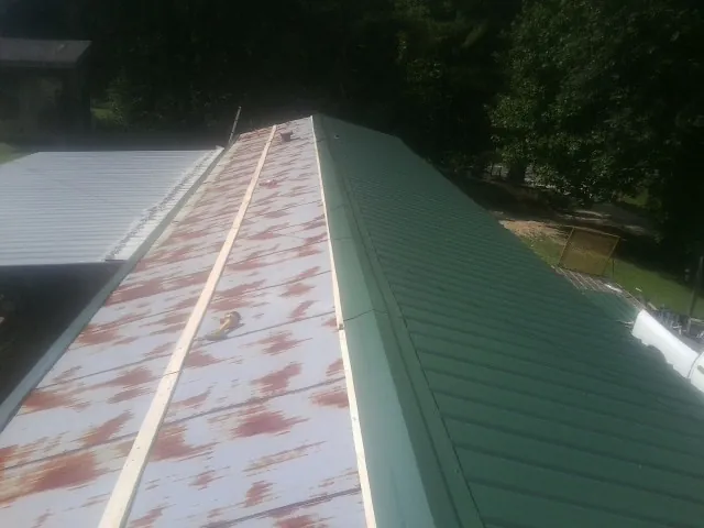 Old rusted panels beside newly installed green metal roofing — Wind Damage Roof Repair by Roofing Brothers in Champion