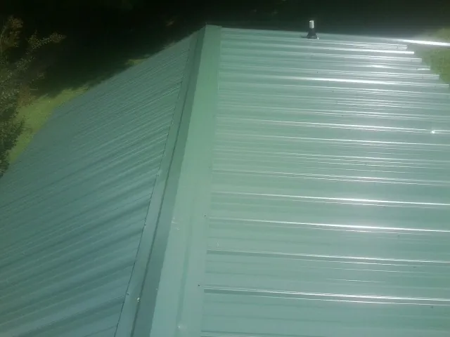 New green metal panels meeting at the ridge of a roof — Flat Roof Repair work by our crew in Champion