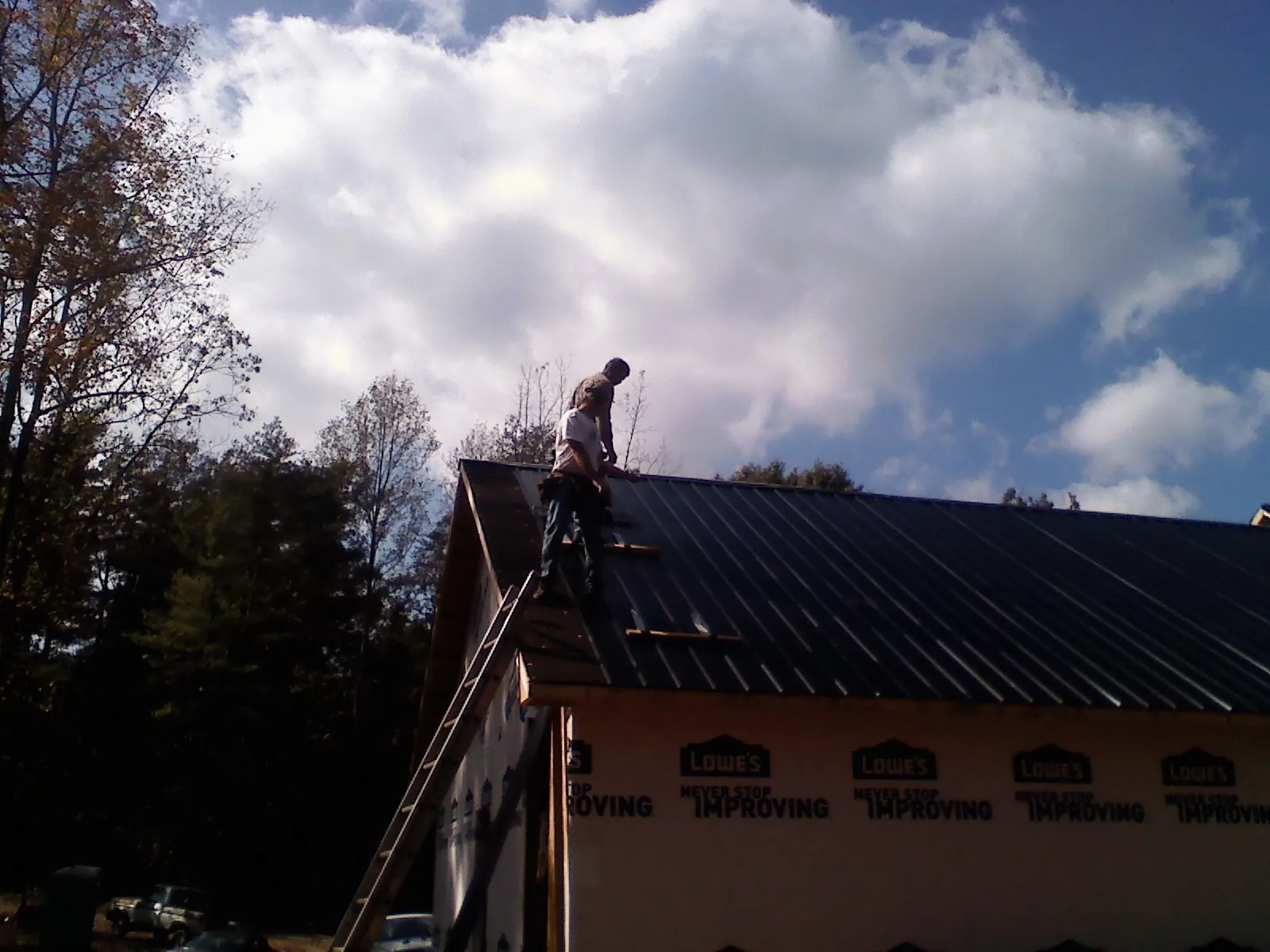 Roofer fastening dark metal panels high against a cloudy sky, from a Roof Inspection job in Champion