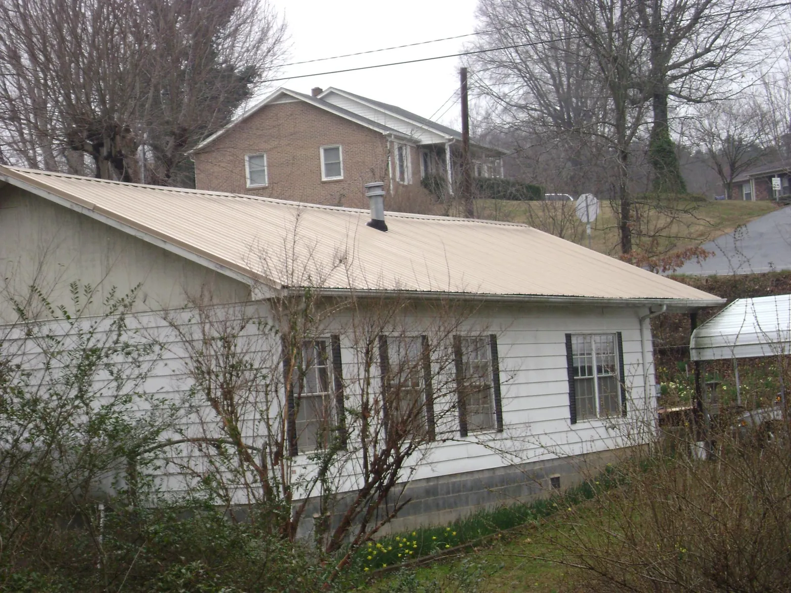 Tan metal roof on a white sided house set into a hillside — Commercial Roofing by Roofing Brothers in Champion