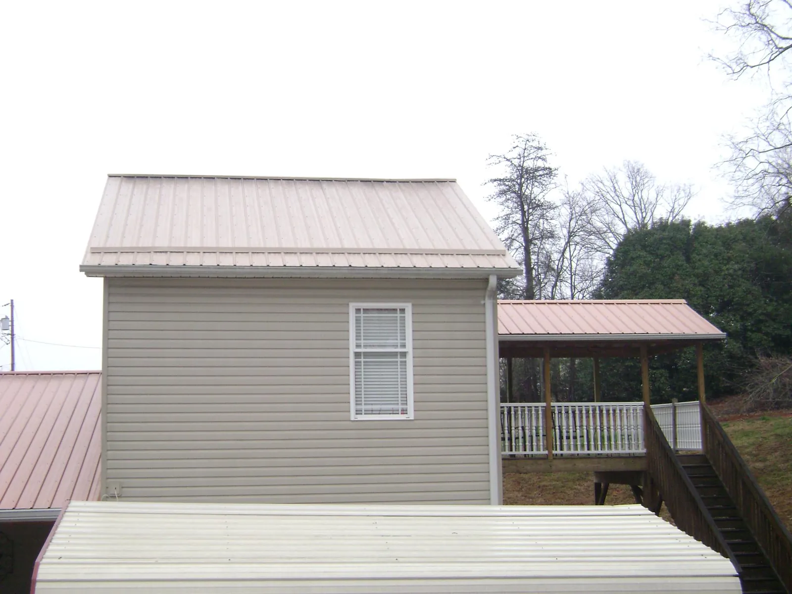 Tan metal roofs on a two story addition and attached porch, from a Roof Replacement job in Champion