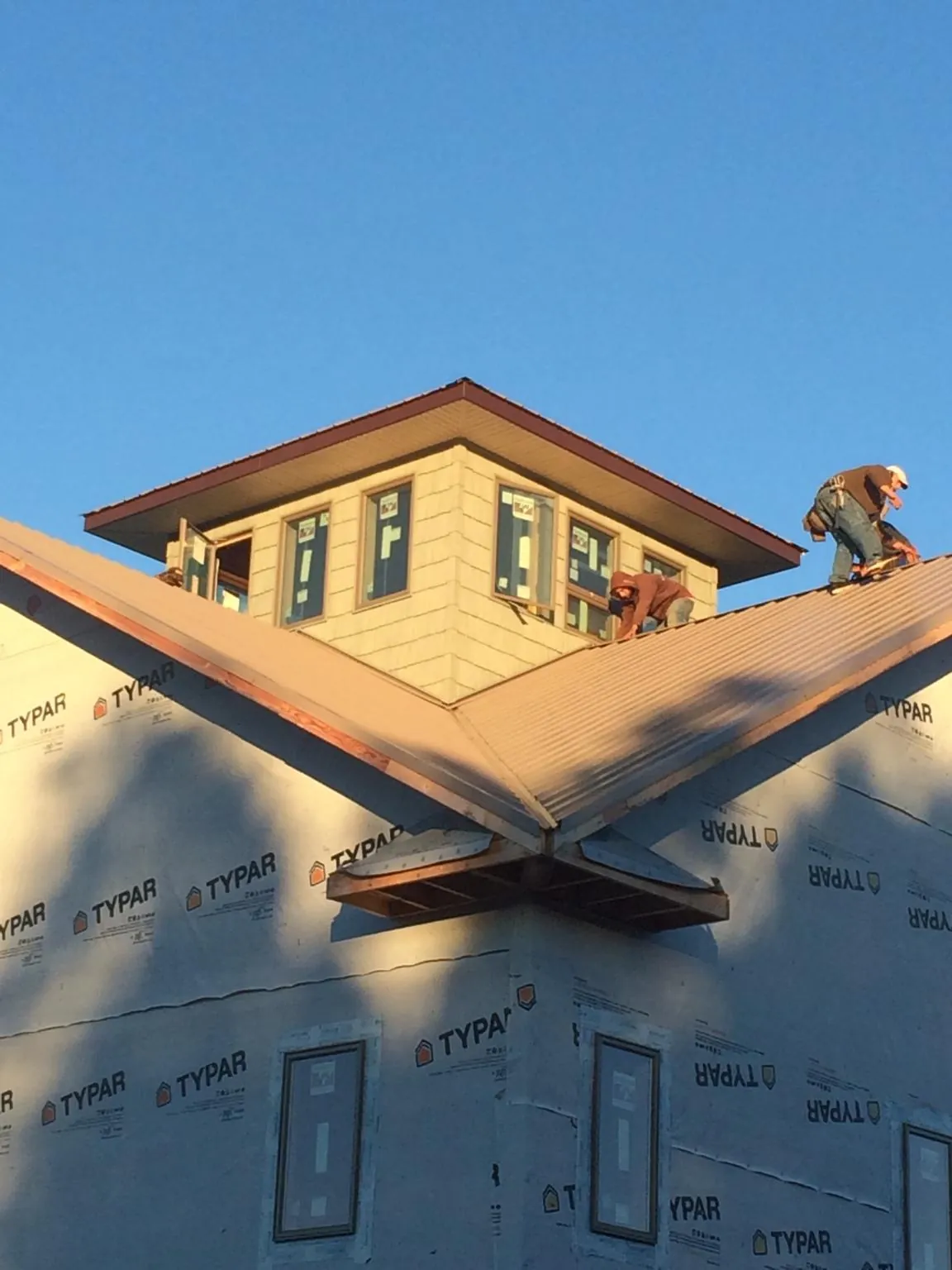 Roofers working around a rooftop cupola on a new metal roof at sunset — Roof Waterproofing in Champion by Roofing Brothers